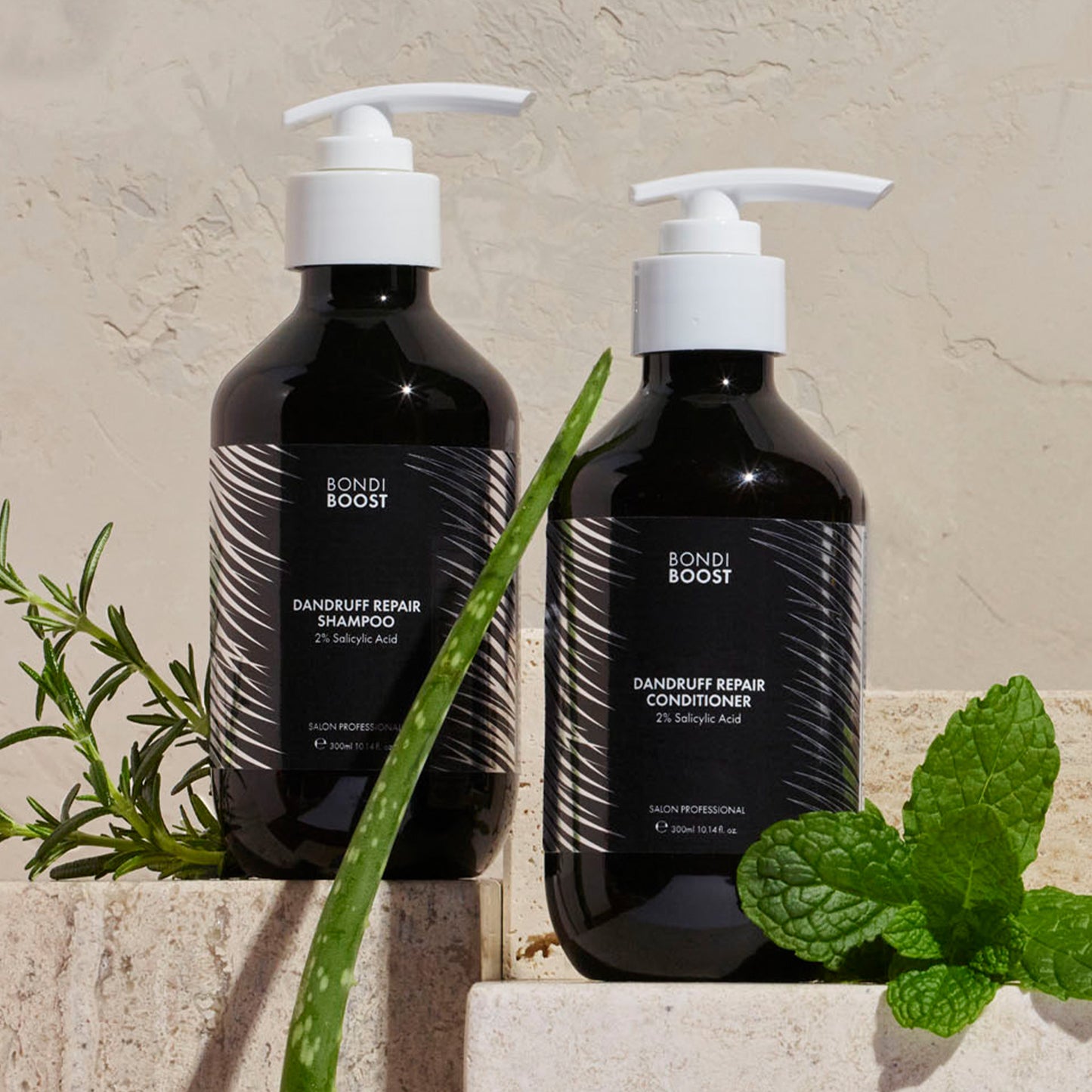 Two black bottles of Bondi Boost dandruff repair shampoo and conditioner with green leaves on a beige background.